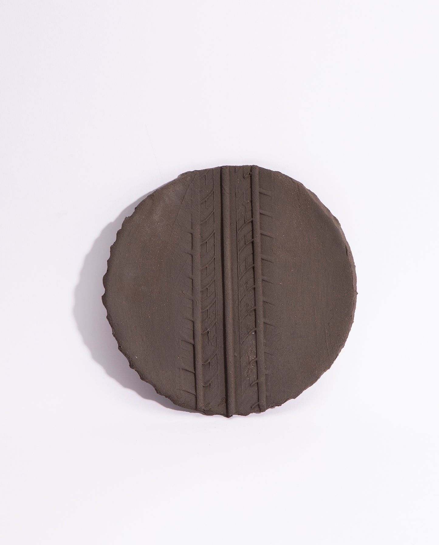assiette en grès noir brute, avec une empreinte de pneu en son milieu