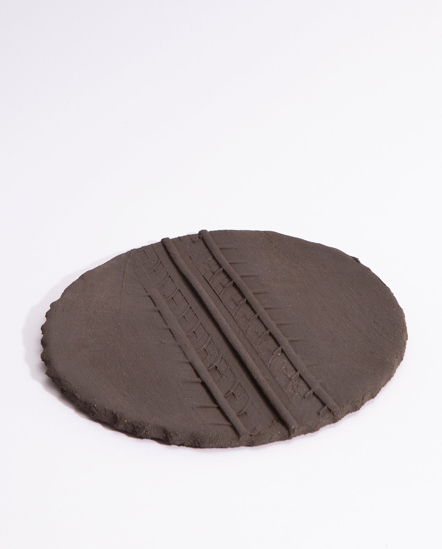 assiette en grès noir brute, avec une empreinte de pneu en son milieu