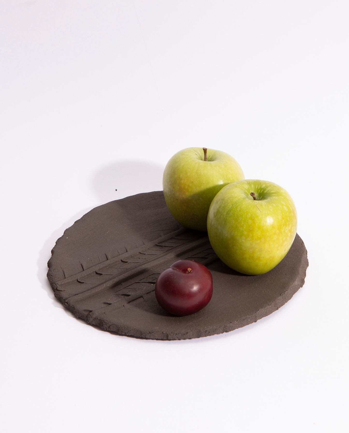 assiette en grès noir brute, avec une empreinte de pneu en son milieu. Ce plat peu contenir des fruits et des légumes.