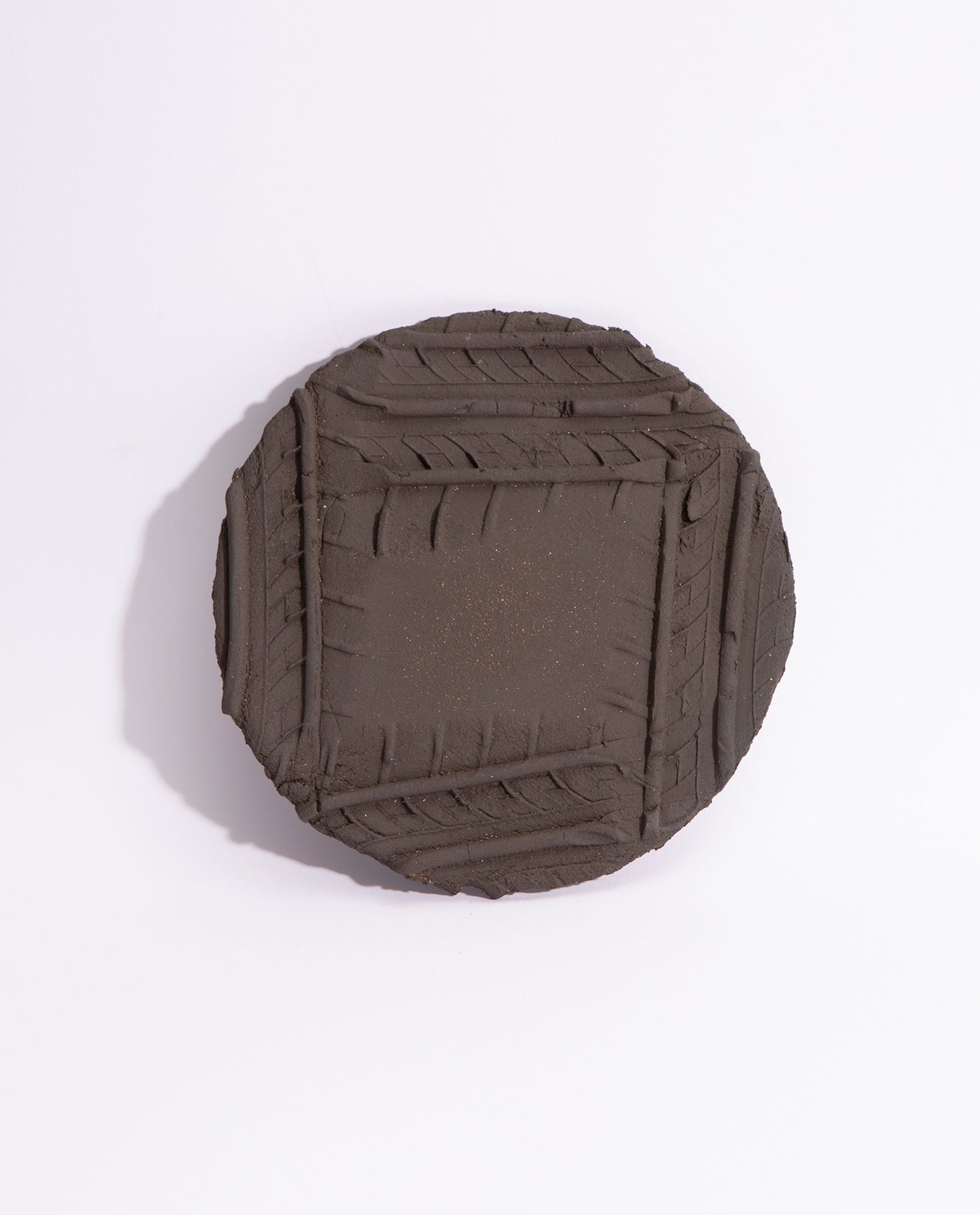 Assiette en grès noir brut, avec quatre empreintes de pneu qui forme un carré sur l'assiette.