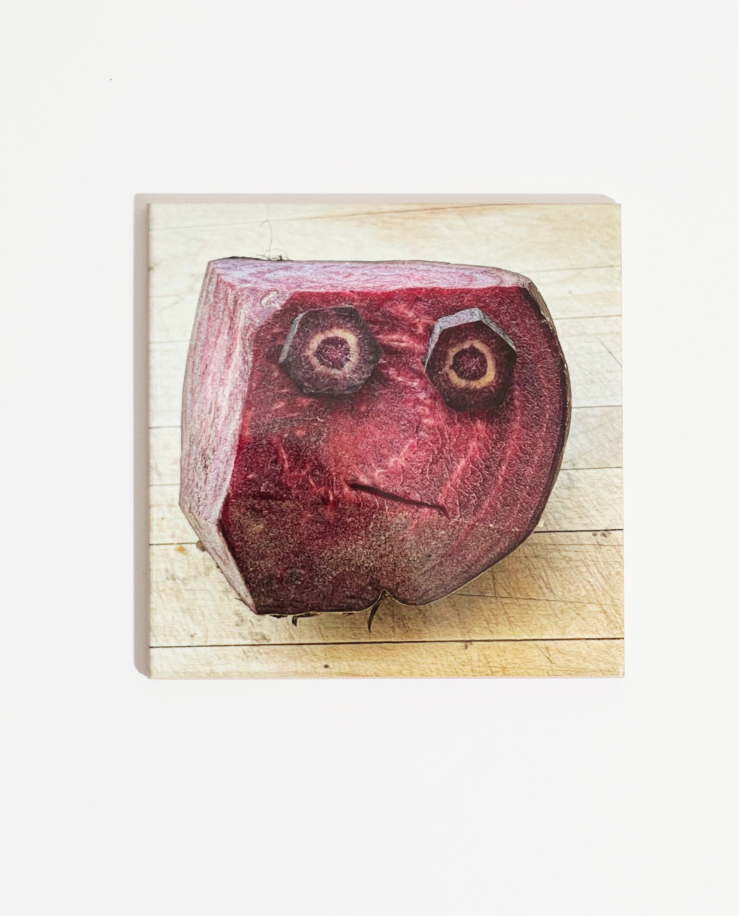 Carreau de faïence imprimée d'une photo de l'artiste Olaf Breuning représentant un visage sur un morceau de bettrave rouge. Celui-ci peut être intégré à une faïence de cuisine ou accroché dans la maison.